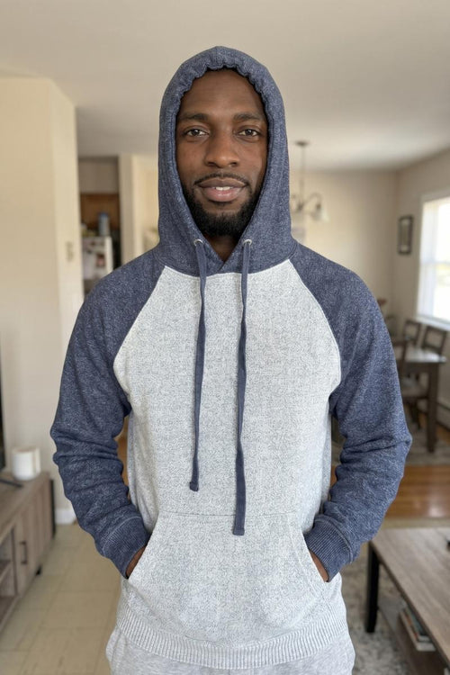 Man wearing a gray and blue hoodie in a living room setting
