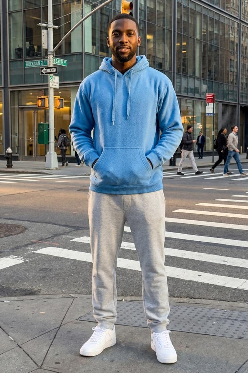 Man wearing a blue hoodie and gray sweatpants standing on a city street.